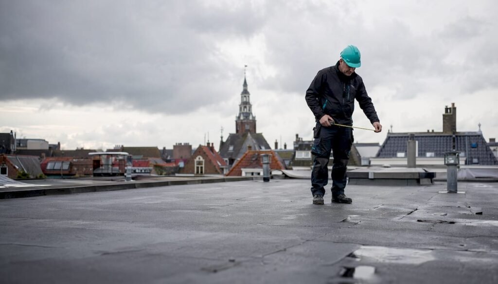 Een dakdekker controleert het bitumen dak op eventuele gebreken.