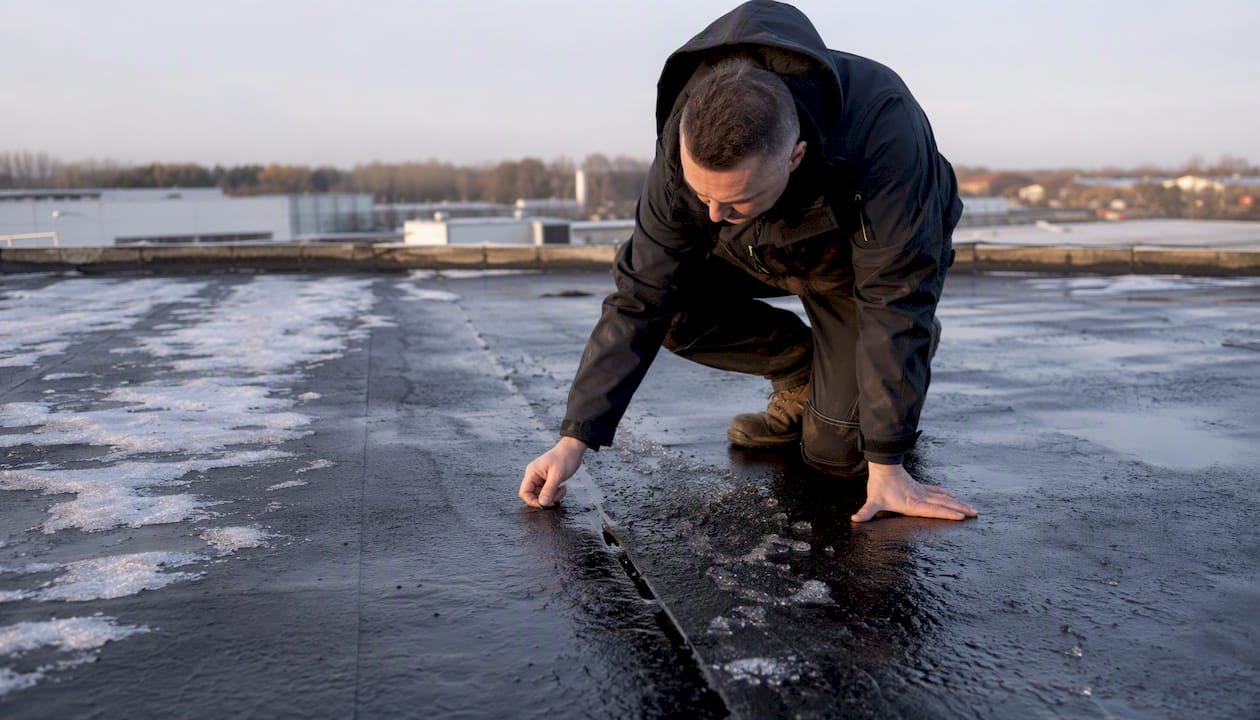 Detailfoto van vorstschade op het dak van een bedrijfspand na een koude winterperiode.