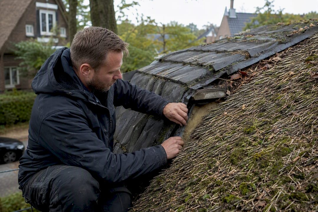 Detailopname van een dakdekker die het dak inspecteert, met focus op zijn handen aan het werk.