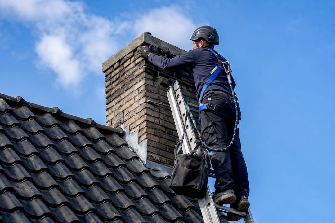 Dakdekker op een ladder repareert de stenen van een schoorsteen