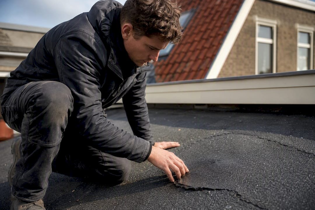 Dakdekker bekijkt schade door blaren op bitumen dak van dichtbij
